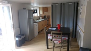 Une cuisine compacte équipée d’un réfrigérateur, d’une cuisinière et d’un évier. On y trouve une table à manger avec des chaises, et une tasse rouge posée dessus.
