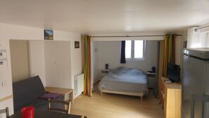 Une chambre à coucher de taille réduite, comprenant un lit, un bureau, une chaise, un radiateur, une fenêtre et un téléviseur.