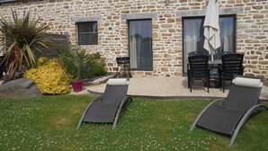 Un edificio in pietra con un patio attrezzato con due poltrone, un tavolo e un ombrellone.
