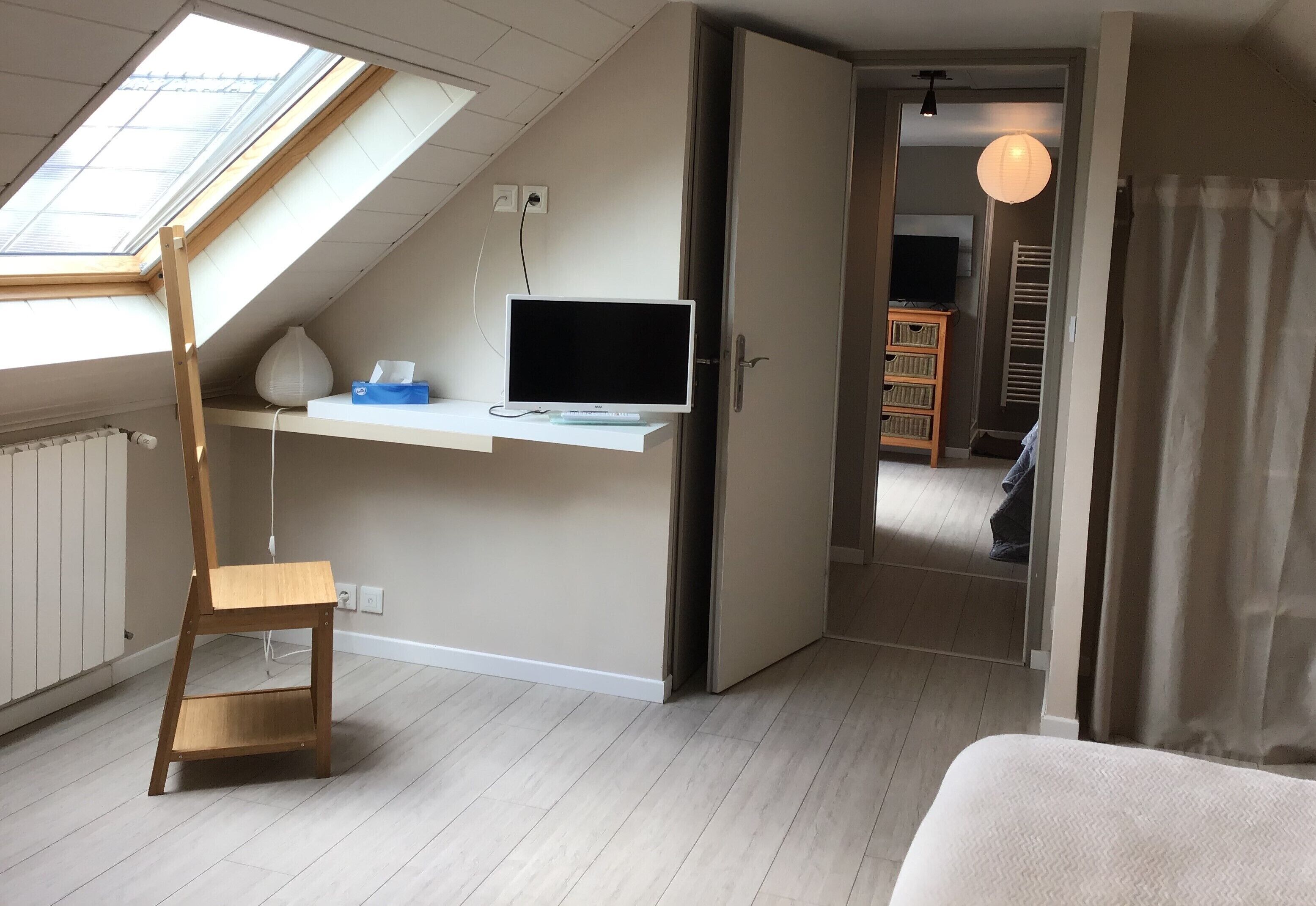 A room with a sloped ceiling, a desk with a computer, a chair, and a bed.