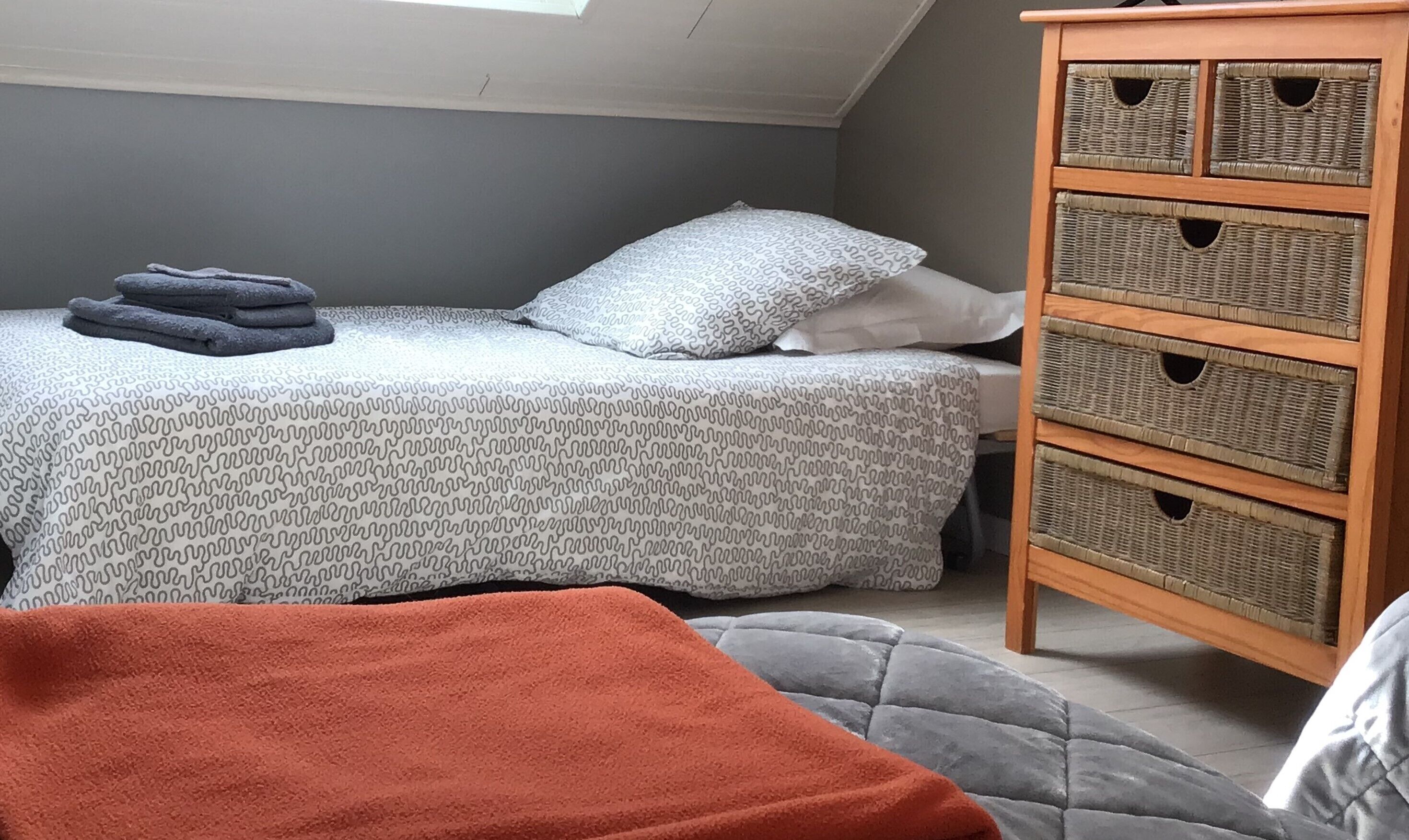 A bedroom with a bed, a chest of drawers, and a skylight.