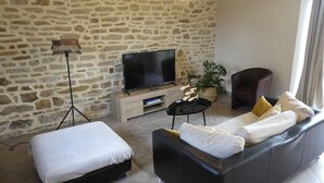 Un soggiorno con parete in pietra, una TV a schermo piatto, un divano, una poltrona e una lampada da terra.