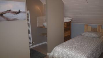 A bedroom with a sloped ceiling, a wooden headboard, a bed with patterned bedding, a white wall-mounted shelf, and a painting of a tree branch.