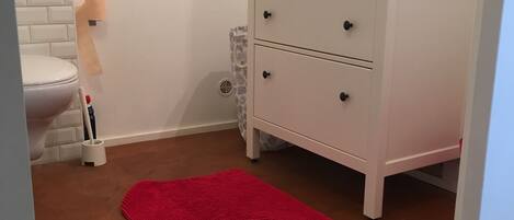 A bathroom with a toilet, a white sink with a mirror, a red rug, and a patterned rug on the floor.