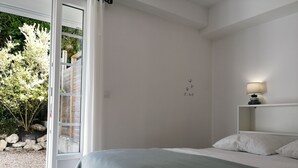 Ein Schlafzimmer mit einem Bett, einem Nachttisch, einer Lampe und Blick ins Freie.