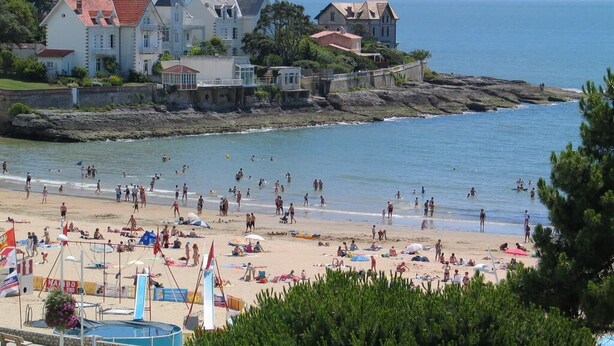Ein Strand mit Personen, einem Pool und Häusern im Hintergrund.