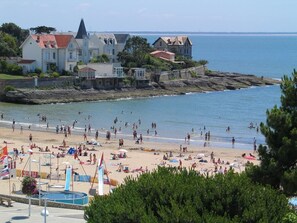 Ein Strand mit Menschen, einem Schwimmbad und Gebäuden im Hintergrund.