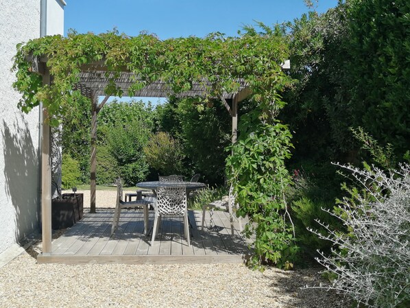 Eine Terrasse mit einer Pergola, Sitzgelegenheiten im Freien und einem Gartenbereich.