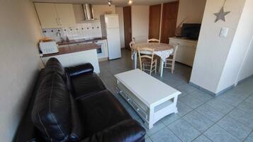 A compact living space with a sofa, a dining table with chairs, a kitchenette, and a star decoration on the wall.