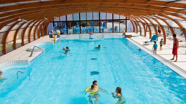 Ein Hallenbad mit Holzbalkendecke und großen Glaswänden.