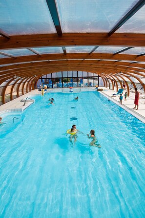 Une piscine intérieure dotée d’un plafond en bois et de murs en verre transparent.