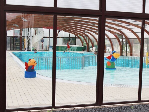 An indoor swimming pool with a covered area, a lifeguard tower, and a children's play area with inflatable toys.
