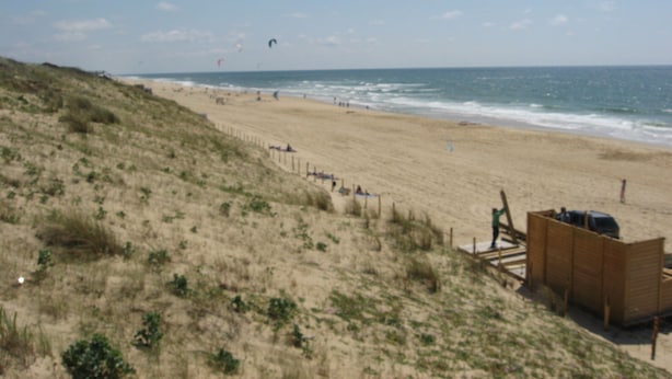 En strand med en trækonstruktion, sandklitter og havet.