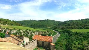 A rural landscape with terraced vineyards, stone buildings with red-tiled roofs, and a river flowing through the valley. - The press house (minerve)