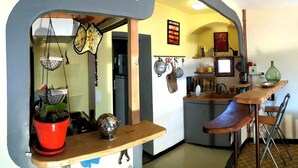 A kitchen with a unique arch design, a wooden bar counter, hanging pots, and a red pot with a plant. - The press house (minerve)