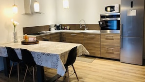A modern kitchen with a stainless steel refrigerator, a microwave, and a built-in oven. There is a dining area with a table and chairs, and a vase with flowers on the counter.