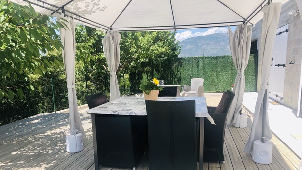 An outdoor patio with a table and chairs, surrounded by a wooden deck and covered by a canopy.