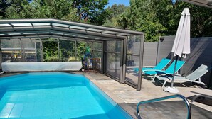 Une piscine entourée de parois en verre, avec des chaises longues et un espace abrité.