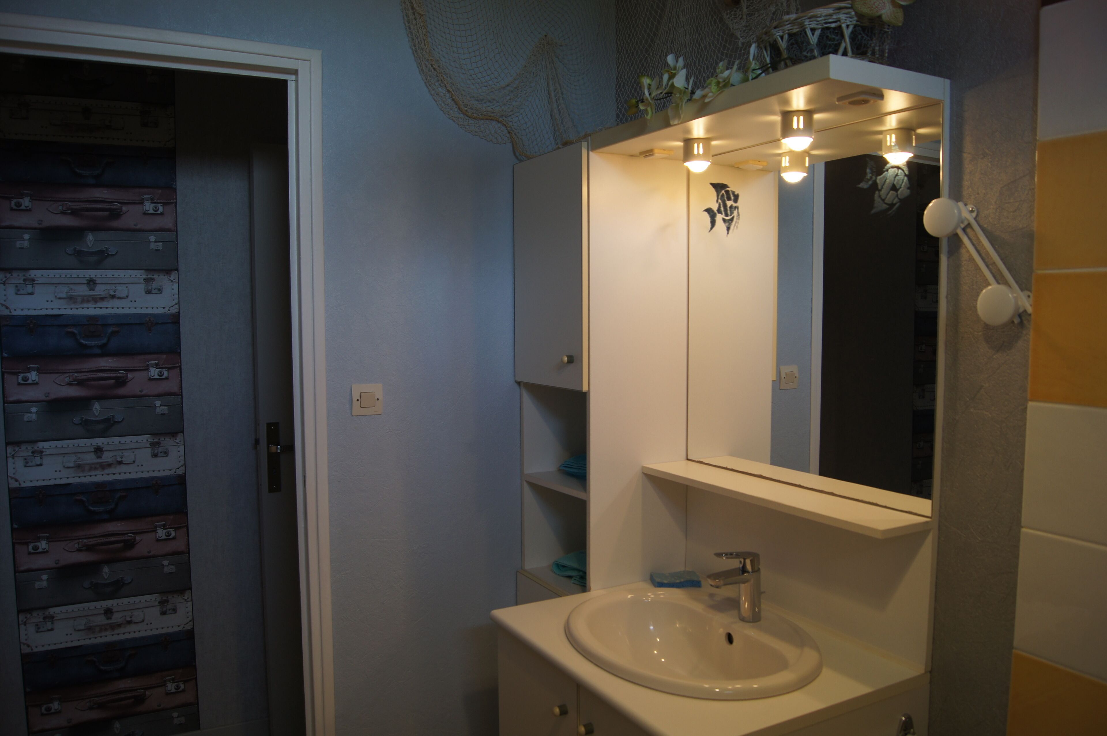 A bathroom with a sink, mirror, and a wall of suitcases.