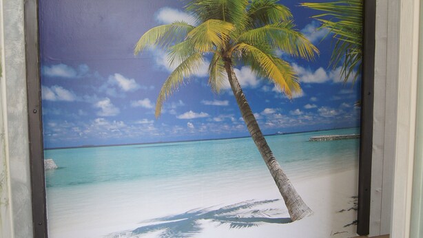 Une pièce dont un mur est décoré d’une fresque représentant une scène de plage, avec des palmiers et un ciel bleu azur.