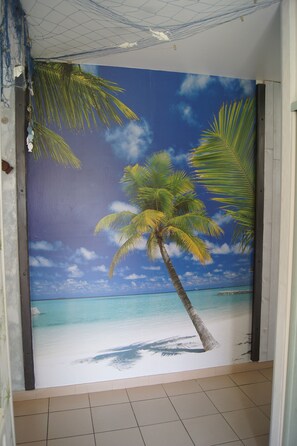 Una habitación con un mural que representa una playa, incluyendo palmeras y un cielo azul despejado.