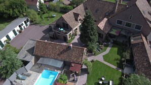 Vue aérienne d’un quartier résidentiel avec une piscine, des pelouses verdoyantes et une maison en briques avec un toit rouge.