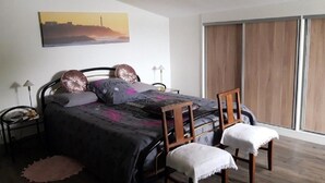 A bedroom with a bed, two bedside tables, a chair, a window with curtains, and a painting on the wall.