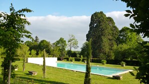 A rectangular swimming pool surrounded by a well-maintained lawn, with trees and shrubs in the background. - Charming guest rooms (Lessac)