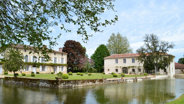 A serene riverside view with historic buildings, a stone wall, and well-maintained greenery. - Charming guest rooms (Lessac)
