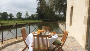 A table set with a white tablecloth, wooden chairs, and a view of a canal with greenery in the background. - Charming guest rooms (Lessac)