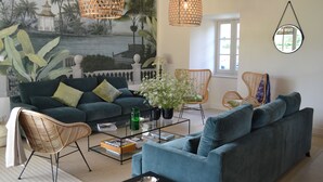 A living room with a green sofa, wicker chairs, a coffee table, and a mural of a tropical scene. - Charming guest rooms (Lessac)