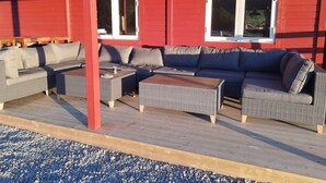 An outdoor seating area with wicker furniture and a red building in the background. - Basecamp Birtavarre (Kåfjord)