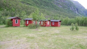 A row of red cabins with sloped roofs, set against a backdrop of a green forest and a mountain. - Basecamp Birtavarre (Kåfjord)