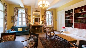 A cozy living room with a fireplace, a sofa, a dining table, and a bookshelf filled with books. - Chateau in magnificent park with swimming pool (Thuir)
