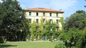 A large, multi-story building with a red-tiled roof, green shutters, and ivy-covered walls. - Chateau in magnificent park with swimming pool (Thuir)
