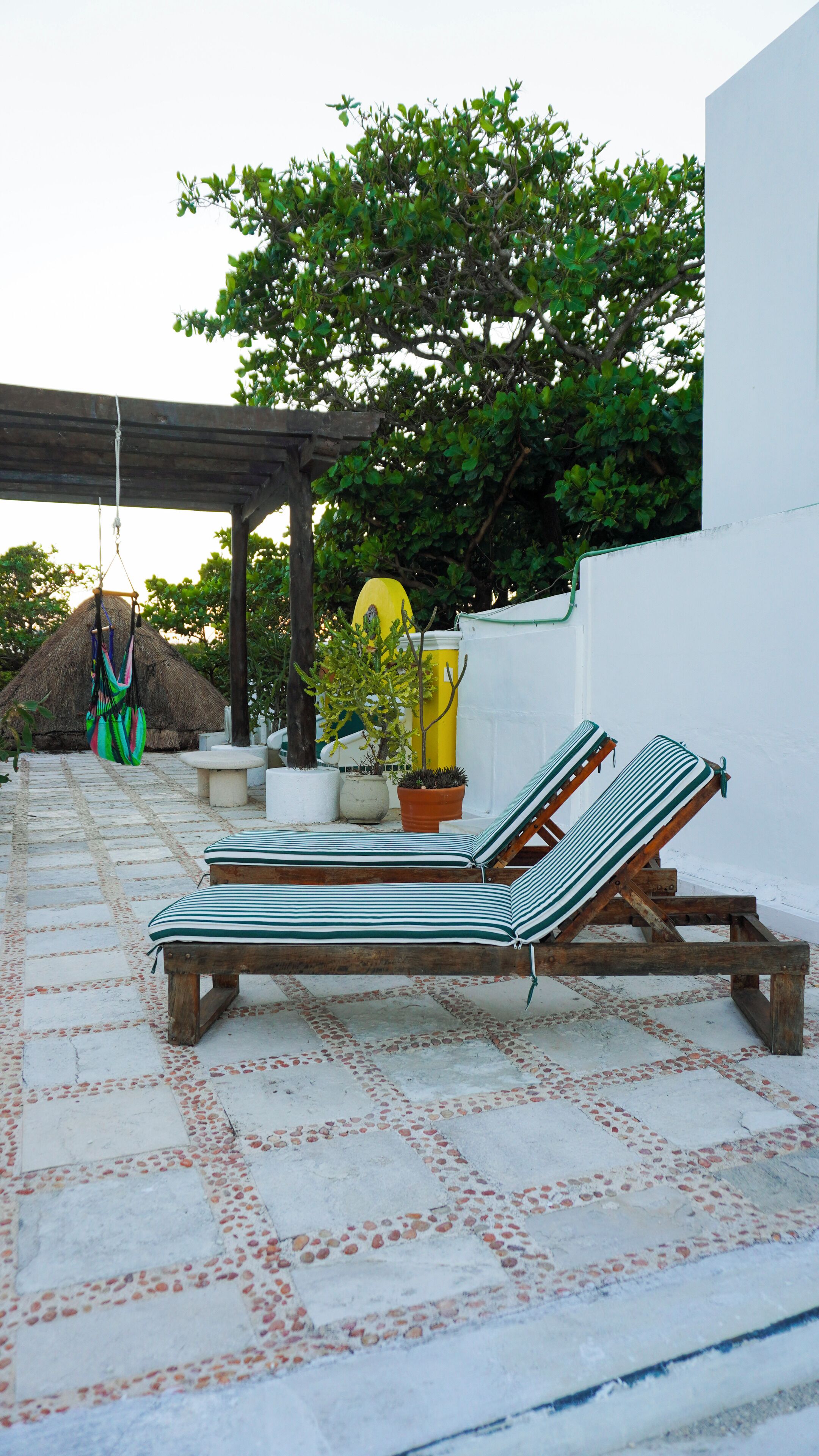 A sunlit outdoor seating area with two lounge chairs, a hanging hammock, and a potted plant.