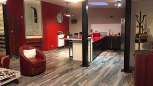 A modern living room with a red sofa, a dining area with a red table, and a kitchen with a red countertop. - Jacques' workshop (Villy)