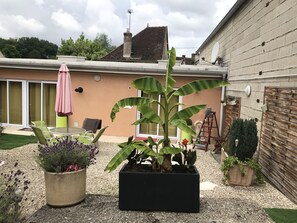 Un patio con una mesa y sillas, una planta en maceta y un edificio con pared de ladrillo y valla de madera.
