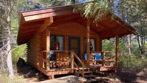 A wooden cabin with a porch, a covered seating area, and a picnic table. - Tamarack Cabin at Columbia Mountain Ranch (Columbia Falls)
