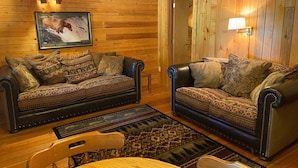 A cozy room with two leather sofas, a wooden dining table, and a patterned rug. - Tamarack Cabin at Columbia Mountain Ranch (Columbia Falls)