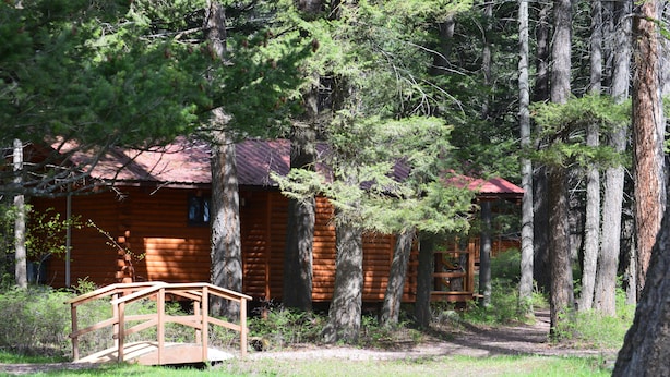 A rustic log cabin surrounded by tall trees. - Tamarack Cabin at Columbia Mountain Ranch (Columbia Falls)