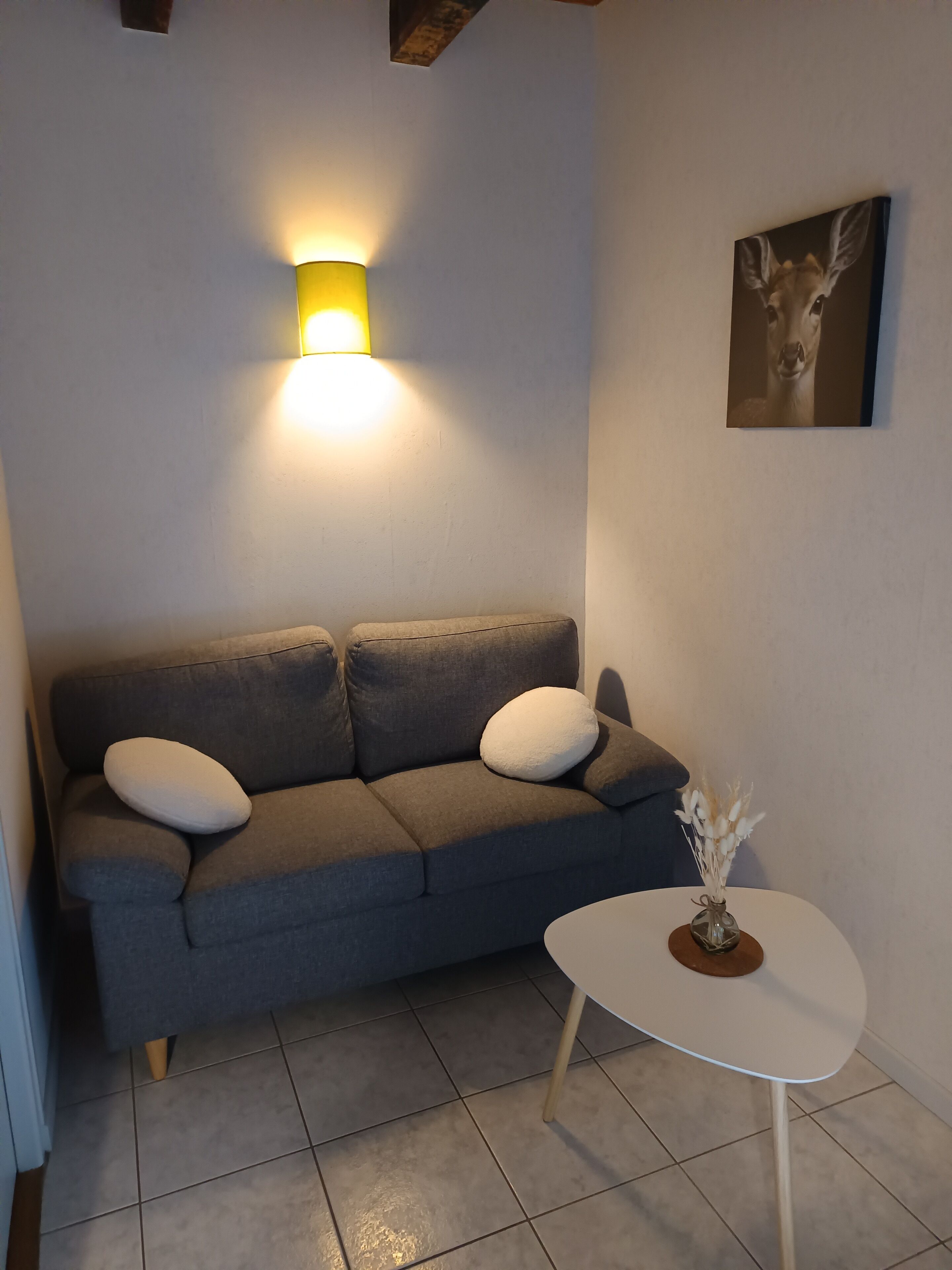 A modern living room with a grey sofa, a small white table, and a wall-mounted lamp.