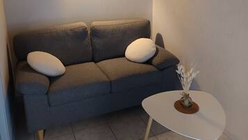 A modern living room with a grey sofa, a small white table, and a wall-mounted lamp.
