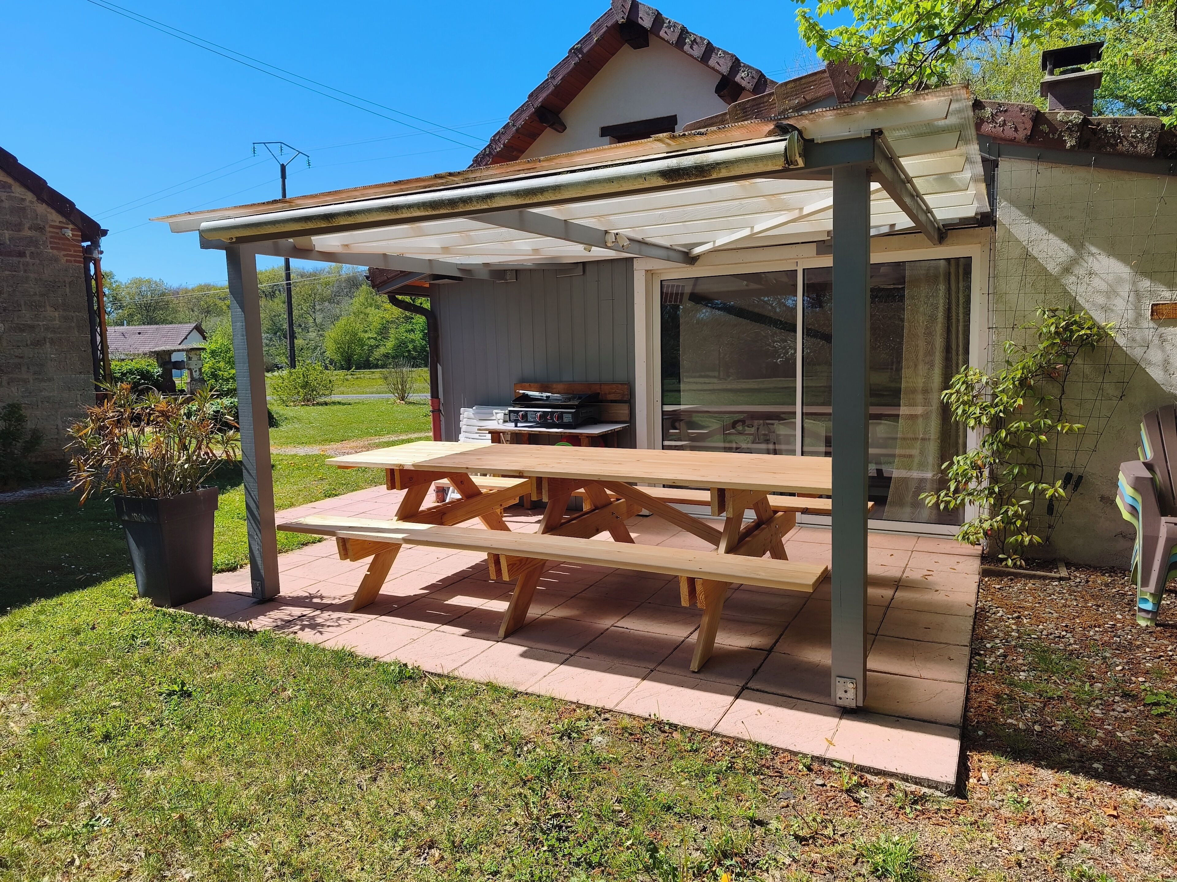 Un espacio de comedor al aire libre techado con una mesa de picnic, una parrilla y una vista de una casa al fondo.