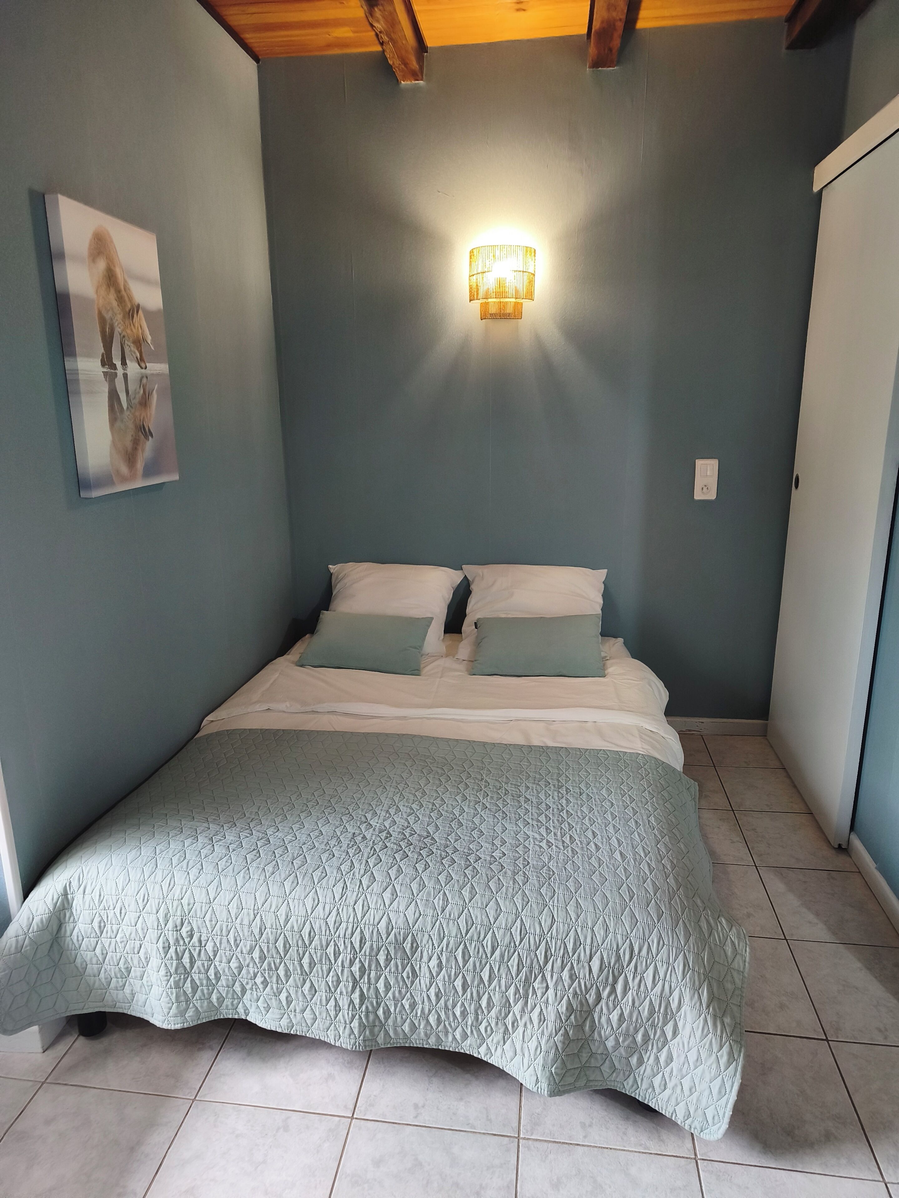 A bedroom with a bed, a wall-mounted light, and a framed picture.