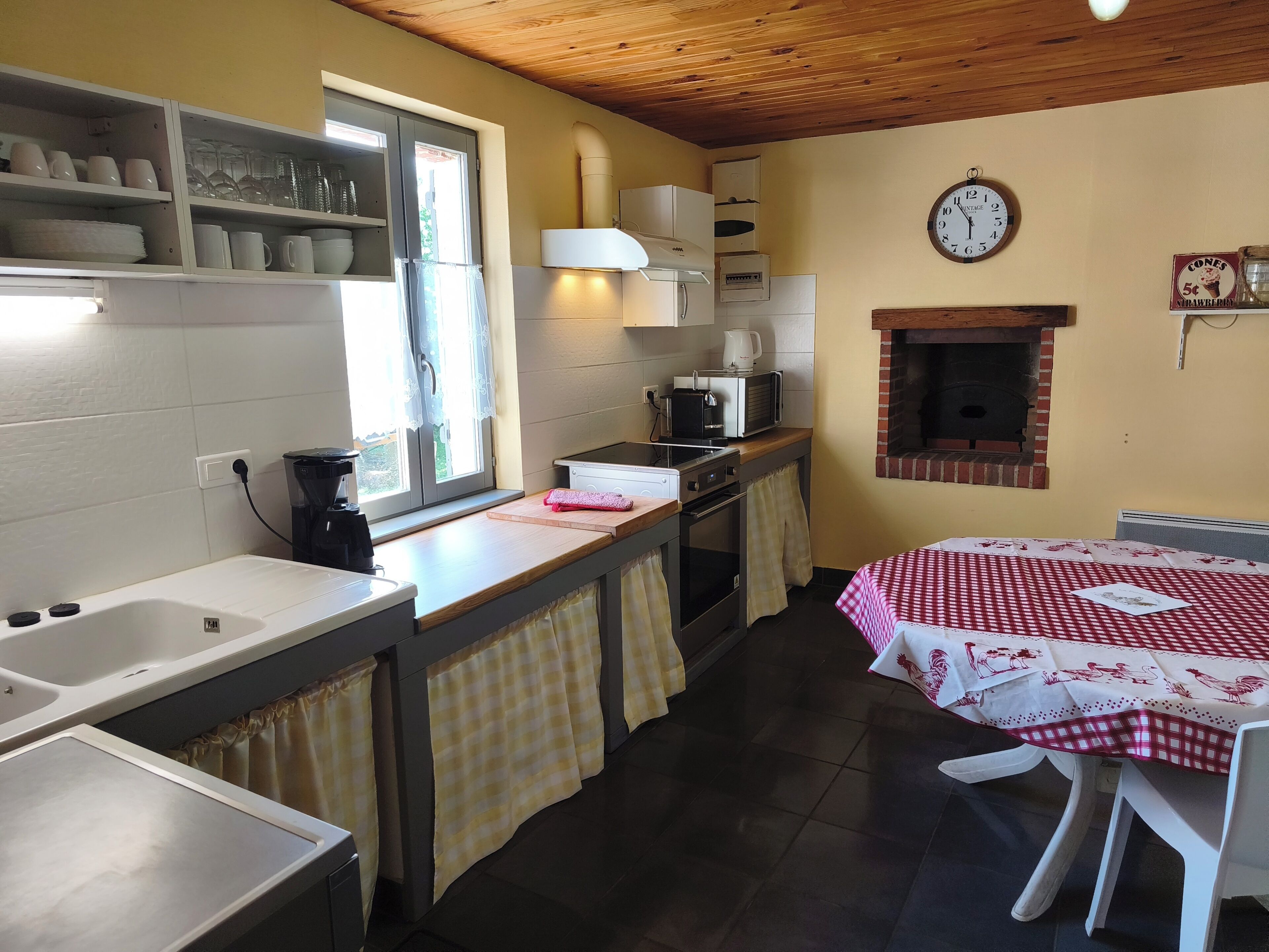 Una cucina con finestra, orologio, microonde, macchina del caffè e forno a mattoni.