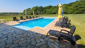 A rectangular swimming pool with a stone deck, surrounded by lounge chairs and umbrellas.