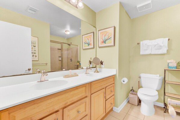 Une salle de bain avec un grand miroir, deux lavabos, des meubles en bois, des toilettes et une douche.