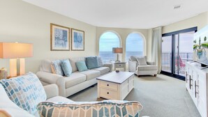 A spacious living room with a sofa, armchairs, a coffee table, and a view of the ocean through arched windows. - Award-Winning Resort Amenities | Seascape 219 (Isle of Palms)