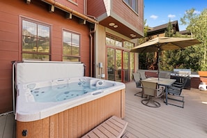 A hot tub on a wooden deck with a table and chairs, and a barbecue grill in the background. - Grand Villa (Crested Butte)